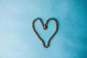 Texture of a beautiful golden dear festive chain of unique weaving in the shape of a heart on a blue background and copy space. Concept love, marriage proposal, marriage, St. Valentine's Day photo