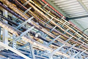 Metal wires in a bunch. Technological tubes on metal stands with tin labels. On the chemical production of unusual structures under the roof. Complex communications. Multicolored metal structures photo