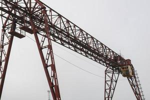 Industrial iron large metal gantry crane with a hook mounted on the supports for lifting and carrying heavy cargo, moving along the rails at the factory. The crane is of bridge type photo