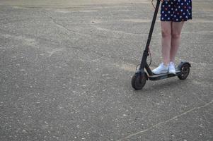 una mujer con falda corta y zapatillas de deporte monta un scooter electrónico moderno de moda con dos ruedas de un aparato de vehículo en una carretera asfaltada alrededor de la ciudad y copia espacio foto