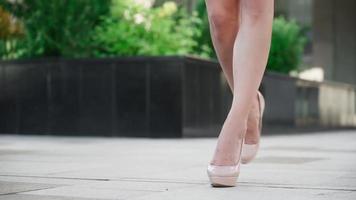 sexig framgångsrik företag kvinna i en rosa klänning gående i de stad parkera. skön kvinna ben i hög hälar är gående längs en urban gata mot de bakgrund av solnedgång ljus. långsam rörelse. video