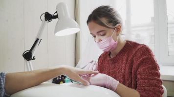 flicka i de rosa nagel tekniker en medicinsk mask och handskar framställning manikyr till en klient på de skönhet salong. de nagel vård. video