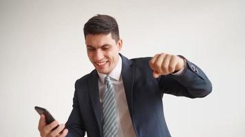 Happy male office worker in formal clothes uses mobile phone and rejoices in victory on white background. Businessman in jacket and tie experiences triumph of the winner, laughs with joy. video