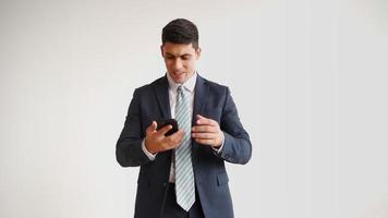 Happy male office worker in formal clothes uses mobile phone and rejoices in victory on white background. Businessman in jacket and tie experiences triumph of the winner, laughs with joy. video