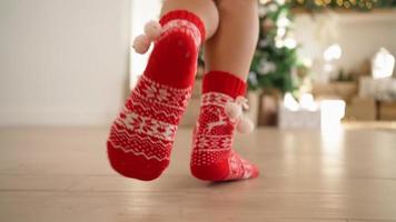 primer plano, mujer feliz con calcetines rojos de año nuevo corre por la sala de luz hasta el árbol de navidad decorado con regalos. año nuevo, ambiente festivo. persona irreconocible. camara lenta. video