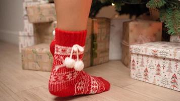 close-up, belas pernas femininas em meias vermelhas de ano novo são adequadas para decorar uma árvore de natal na ponta dos pés. ano novo, atmosfera de inverno, luz quente. Humor festivo. video