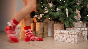 close-up, belas pernas femininas em meias vermelhas de ano novo são adequadas para decorar uma árvore de natal na ponta dos pés. ano novo, atmosfera de inverno, luz quente. Humor festivo. video