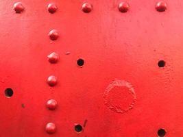 Red iron metal rough painted strong solid industrial wall with rivet holes and bolts. Background, texture photo