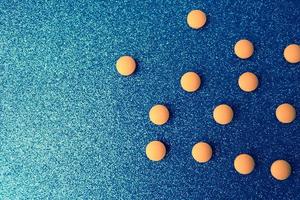 Small yellow orange beautiful medical pharmaceptic round pills, vitamins, drugs, antibiotics on a blue background, texture. Concept medicine, health care. Flat lay, top view photo