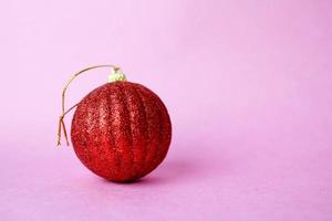 rojo pequeño vidrio redondo plástico invierno inteligente brillante decorativo hermosa navidad festiva bola de navidad, juguete de navidad enyesado sobre destellos sobre un fondo rosa púrpura foto