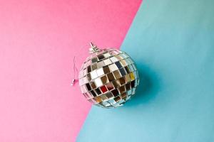 Silver mirror musical club disco ball small round glass winter shiny decorative beautiful xmas festive Christmas ball, Christmas toy plastered on glitter on a gray pink purple background photo