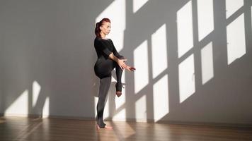 atletisk kvinna i overall håller på med yoga och stretching på en vit bakgrund i ljus solljus. långsam rörelse. video