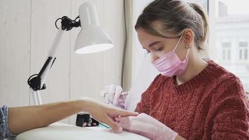 mädchen in den rosa nageltechnikern eine medizinische maske und handschuhe, die maniküre für einen kunden im schönheitssalon machen. die Nagelpflege. video