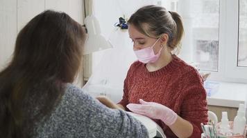 girl in the pink nail technicians a medical mask and gloves making manicure to a client at the beauty salon. The nail care. video