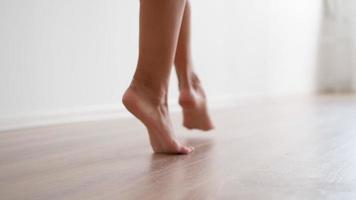 Nahaufnahme, schlanke weibliche nackte Füße gehen vor dem Hintergrund einer weißen Wand. attraktive beine eine nicht erkennbare frau geht anmutig auf zehenspitzen durch die wohnung. fuß- und körperpflegekonzept. video