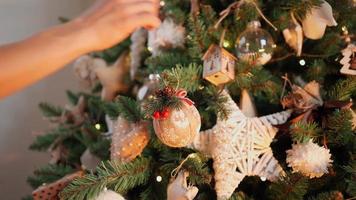 primer plano, una mujer irreconocible decora un árbol de navidad con bolas festivas. luces cálidas de guirnaldas parpadean en el fondo. vacaciones año nuevo. ambiente invernal, concepto de tradición. video