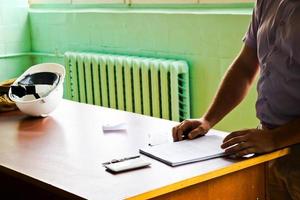A man working engineer with a white helmet on the desk learns to write in a notebook photo