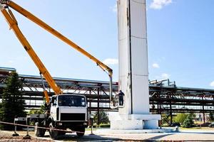 Repair columns on a special technique. Workers on the crane repair a large white column. Cosmetic repair with painting. Workers in a special form paint a column photo