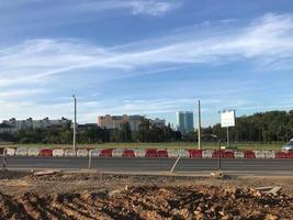 a sandy road is being built in a new area. a new asphalt road is being laid in a modern area of the city. an artificial fence protects people from danger. against the blue sky photo