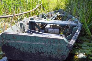 viejo barco roto de madera en mal estado para nadar a orillas del río, lago, mar en la hierba y juncos en la naturaleza foto