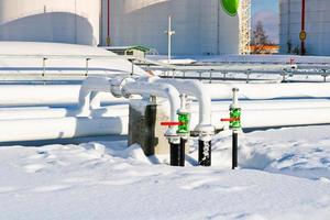 Large white iron metal industrial tanks for storage of fuel, gasoline and diesel and pipeline with valves and flanges at the refinery in the winter photo