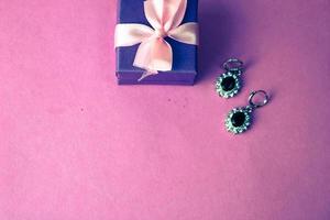 Beauty box, festive beautiful gift box with a bow with silver earrings with precious stones on a pink purple background. Flat lay. Top view photo