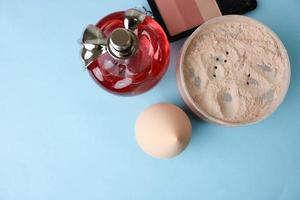 Beauty box, loose matte mineral powder and blush with a beauty blender for makeup and red glass bottle of perfume on a blue background. Flat lay. Top view photo