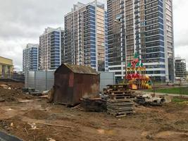 a small rusty garage stands in the center of a new residential complex. the rusty house stands against the backdrop of blue-and-white glass tall apartment buildings. urban landscape photo