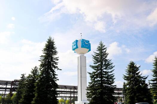 reloj inusual sobre un fondo de un cielo blanco-azul. un reloj en forma de molécula, un átomo. sobre la producción química, una columna de vigilancia, una torre de reloj en un bosque de abetos. telón de fondo de tuberías químicas foto