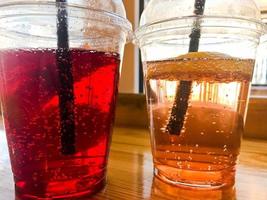 Two glasses of plastic red and yellow refreshing cold tasty sweet raspberry strawberry cherry orange peach lemon fruit lemonade natural with a straw and syrup bubbles photo