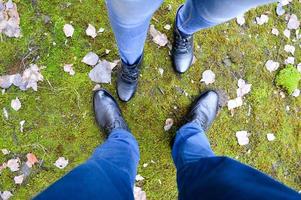 Boots of a man and a woman against a background of green moss and autumn leaves. Male and female legs. Socks are directed apart. photo