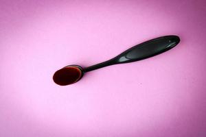 Wooden brush made of natural lint for applying tone on a purple and pink background. Flat lay. Top view photo