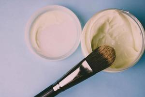 A beauty box with a wooden brush made from natural hard lint for a tone and a round jar of cream, a make-up base with a second skin effect on a blue background. Flat lay. Top view photo