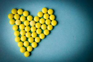 Small medical pharmaceptic round yellow pills, vitamins, drugs, antibiotics in the form of a heart on a blue background, texture. Concept medicine, health care, heart disease. Flat lay, top view photo