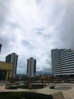 urban landscape with tall glass buildings and blue tenement houses. columns of houses, next to a house of blue and white in the form of a wave. there is a long mall and benches nearby photo