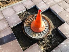 un cono naranja se encuentra en una sección peligrosa de la carretera. la marca de identificación en un color brillante y distintivo se encuentra en un agujero en el camino. la superficie de la carretera se desplaza foto