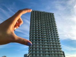 a tall white house made of aerated concrete. with panoramic glazing, in Arabic style with terraces. girl holding fingers, measuring the size of the house. blue creative manicure on nails photo