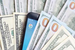 KHARKIV, UKRAINE - MAY 2, 2021 Smartphone screen with Google app and lot of hundred dollar bills. Business and social networking concept photo