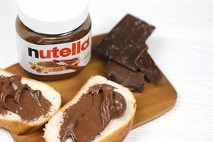 kharkov, ucrania - 27 de diciembre de 2020 lata de vidrio de nutella y untada en pan recién horneado. nutella es fabricada por la empresa italiana ferrero introducida por primera vez en 1964 foto