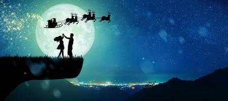 silueta de santa claus en la noche de navidad con pareja bailando bajo la luna llena. foto