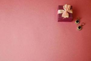 Beauty box, festive beautiful gift box with a bow with silver earrings with precious stones on a pink purple background. Flat lay. Top view photo