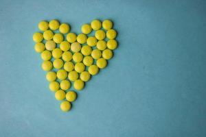 Small medical pharmaceptic round yellow pills, vitamins, drugs, antibiotics in the form of a heart on a blue background, texture. Concept medicine, health care, heart disease. Flat lay, top view photo