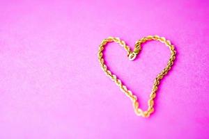 Texture of a beautiful golden festive chain unique weaving in the shape of a heart on a pink purple background and copy space. Concept love, marriage proposal, marriage, St. Valentine's Day photo