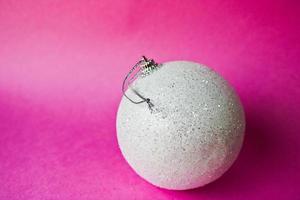 White small round glass plastic winter smart shiny decorative beautiful xmas festive Christmas ball, Christmas toy plastered over sparkles on a pink purple background photo