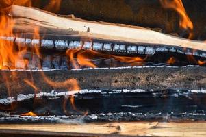 tablones de madera quemados calientes carbonizados de troncos de madera en un fuego con lenguas de fuego y humo. textura, fondo foto