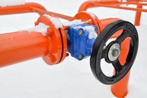 Industrial shut-off regulating protective pipe fittings. Black valve for opening, closing on an iron orange metal pipe with flanges, studs, nuts against the background of white snow in winter photo