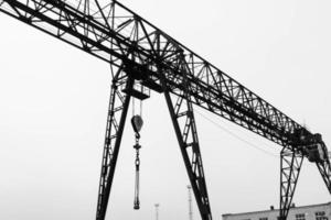 grúa de pórtico de metal grande de hierro industrial con un gancho montado en los soportes para levantar y transportar carga pesada, moviéndose a lo largo de los rieles en la fábrica. la grúa es de tipo puente foto