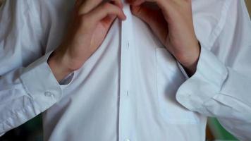 Mens, mannelijk, jongen, detailopname knopen zijn shirt. een Mens bereidt zich voor naar iets gaan ergens. detailopname van handen knopen zijn shirt. video