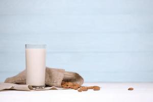 Glass of almond milk with almond nuts on canvas fabric on white wooden table. Dairy alternative milk for detox, healthy eating and diets photo