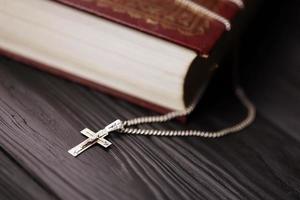 collar de plata con cruz crucifijo en el libro de la santa biblia cristiana sobre una mesa de madera negra. pidiendo bendiciones de dios con el poder de la santidad, que trae suerte foto
